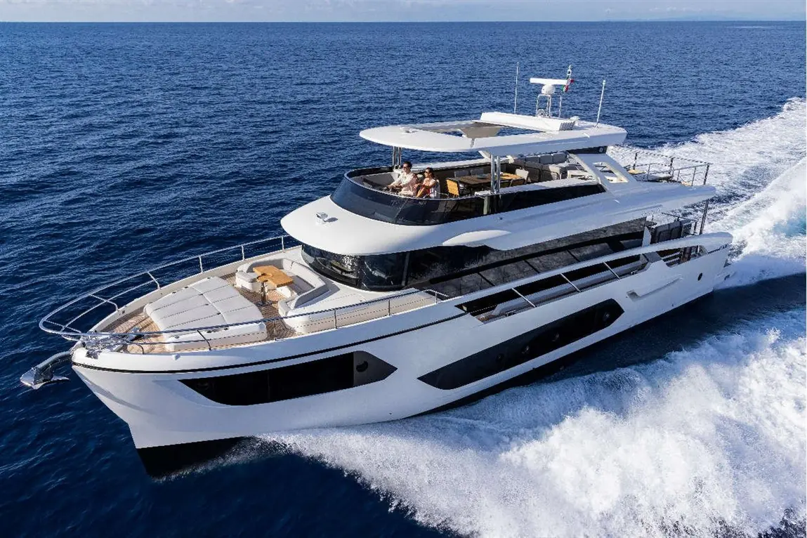 Luxury yacht cruising through deep blue waters, with two people on deck enjoying the sun and scenery.